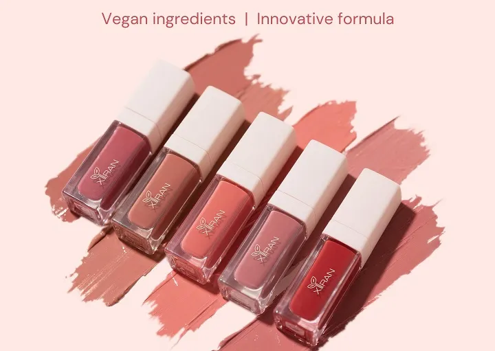 Five shades of vegan lipstick in bottles with smudged swatches in background.
